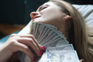 Young Woman Lying In Bed With Money In Her Hands